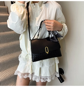 Dettaglio borsa nera a trama intrecciata con fibbia dorata e foulard decorativo in seta