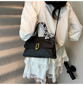 Dettaglio borsa nera con trama intrecciata, chiusura dorata e sciarpa di seta decorativa