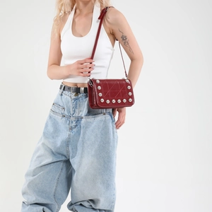 Borsa a tracolla punk trapuntata rosso scuro con borchie argentate indossata da modella