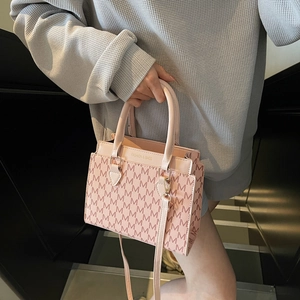 Sac à main rose avec imprimé monogramme et bandoulière amovible près d'un escalier design