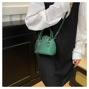 Detail of dark green crocodile texture handbag with gold zipper and adjustable shoulder strap
