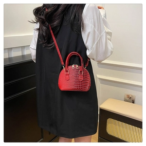 Detail of red crocodile pattern shell bag worn crossbody in a minimalist home setting