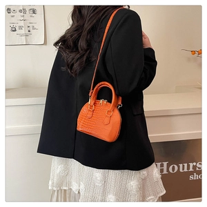 Model wearing a bright orange mini shell bag with crocodile texture and metallic zippers