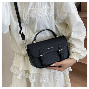 Close-up of black lychee grain leather saddle bag with double buckles and top handle