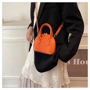 Detail of orange crocodile-pattern shell bag with dual metal zippers and handle