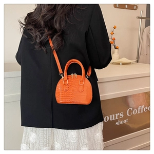 Close-up of bright orange shell bag with crocodile texture and gold hardware details