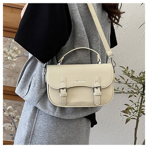 Detail of beige lychee textured saddle bag featuring silver buckles and fashion logo