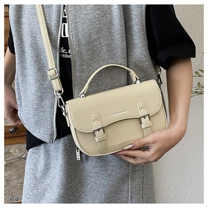 Close-up of litchi grain cream saddle bag featuring double strap pin buckles and handle