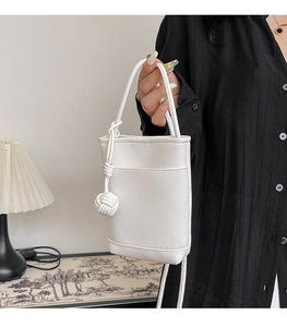 Détail d'un mini sac seau en cuir grainé blanc avec un pendentif boule tissé élégant