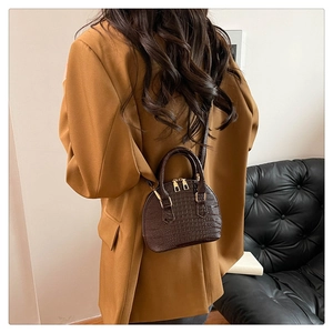 Detail of a dark brown crocodile pattern shell bag worn as a stylish crossbody bag