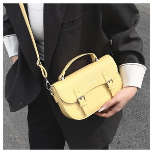Street style shot of a bright yellow pebbled leather saddle bag with silver buckles
