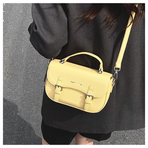 Detail of yellow lychee leather handbag with metal buckles on model with grey suit