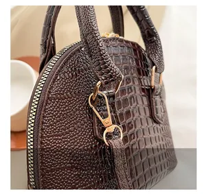 Detail of dark brown crocodile embossed texture and golden hardware on the shell handbag