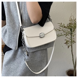 Detail of white grain leather saddle bag with silver buckle and chain on a model