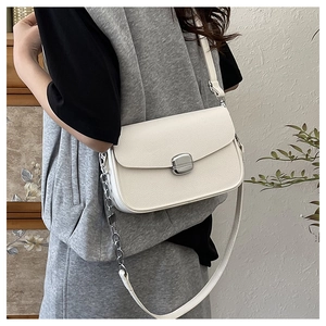 Detail of white lychee leather saddle bag with silver buckle and chain strap on model