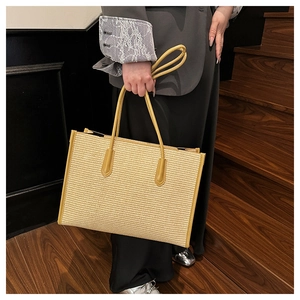 Detail view of woven straw tote bag texture and faux leather handles on female model