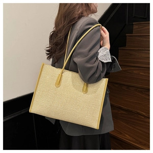 Detailed view of a beige woven tote bag with vibrant yellow leather handles and trim