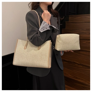Detail view of woven straw tote bag with brown leather trim and matching inner pouch