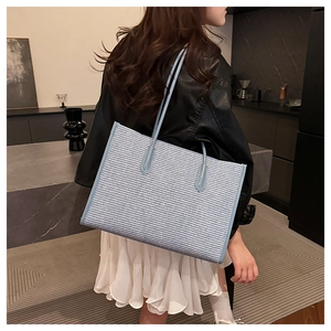 Detail of light blue woven tote bag with slim leather handles worn over the shoulder