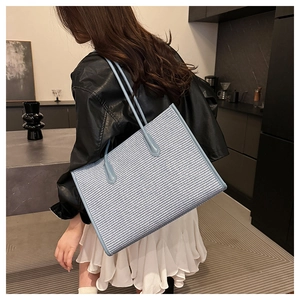 Close-up of a blue tweed woven tote bag showing texture and leather shoulder strap