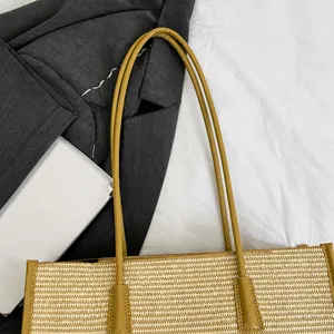 Detailed view of beige straw tote bag with khaki leather trim on white bedding