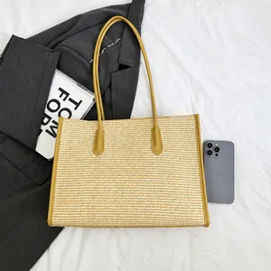 Large straw tote bag with brown leather handles shown next to a smartphone for scale