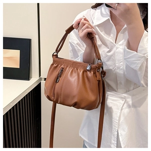 Detail of brown pleated leather handbag with metallic zipper and textured lychee grain finish