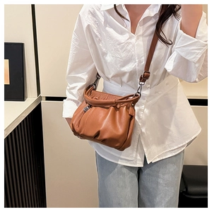 Brown lychee textured crossbody bag with soft pleated design worn by a model in a room