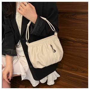 Close-up of cream textured leather bucket bag with metallic zipper and drop pendant detail