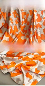 Close-up detail of smooth satin scarf showing orange abstract print and fine edge stitching