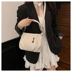 Close-up of beige ruched bucket bag with litchi texture on a model wearing a blazer