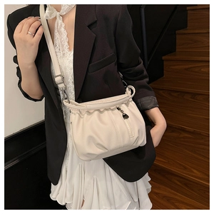 Detail view of cream white pebbled leather handbag with heart charm and shoulder strap