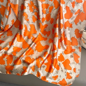 Silk satin beach scarf with orange abstract patterns and elegant draped texture