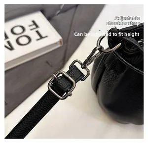 Detail of adjustable leather shoulder strap with dark gray metal buckle on a black bucket bag