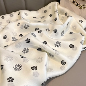 Detailed texture of white silk scarf with black camellia prints on leather surface