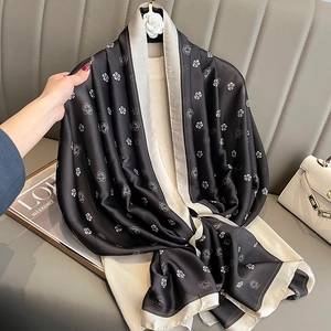 Elegant black silk-like camellia print scarf with beige borders on a beige sweater