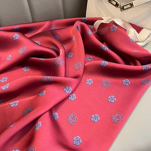 Detailed view of red silk scarf featuring blue camellia patterns on leather surface