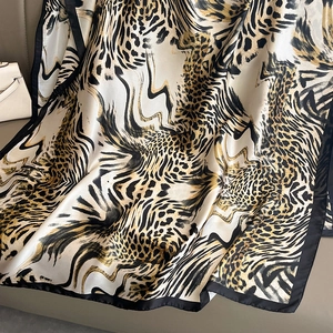 Elegant leopard print silk scarf with black hem displayed on a luxury leather background