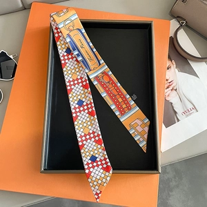 Detail view of a French plaid silk twilly scarf over an orange gift box with illustrations