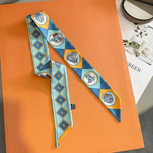 Close-up of a geometric animal print twilly silk scarf draped over an orange box