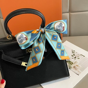 Black leather handbag with orange printed silk scarf tied on the handle and gold hardware