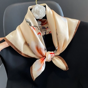 Elegant champagne silk scarf with orange floral prints hanging on a golden hook