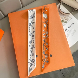 Detail view of long silk scarves with chain print on an orange box with magazine