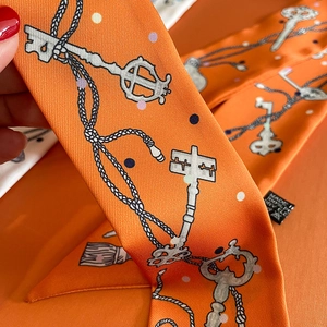 Close-up of silk twilly scarf with vintage key patterns and orange gift box packaging