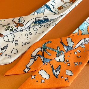 Close-up of narrow silk twill scarves with nautical anchor and bird prints on orange background