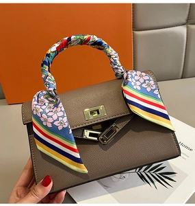 Detail eines Seidenschals am Griff einer braunen Ledertasche mit goldenem Drehverschluss
