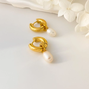 Détail de boucles d'oreilles créoles dorées avec perles d'eau douce baroques sur fond blanc