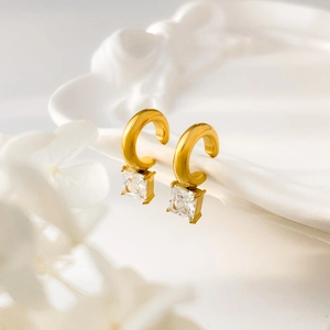Gros plan de boucles d'oreilles dorées avec zircon carré sur plateau blanc décoré