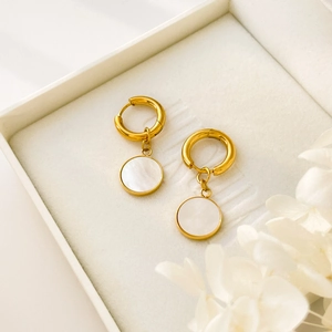 Boucles d'oreilles pendantes dorées avec pendentifs ronds en nacre blanche sur un écrin blanc