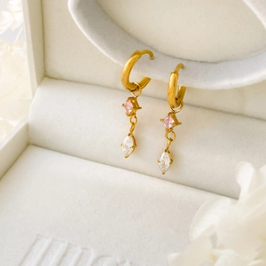 Détail de créoles dorées avec zircon rose carré et pierres blanches taille marquise